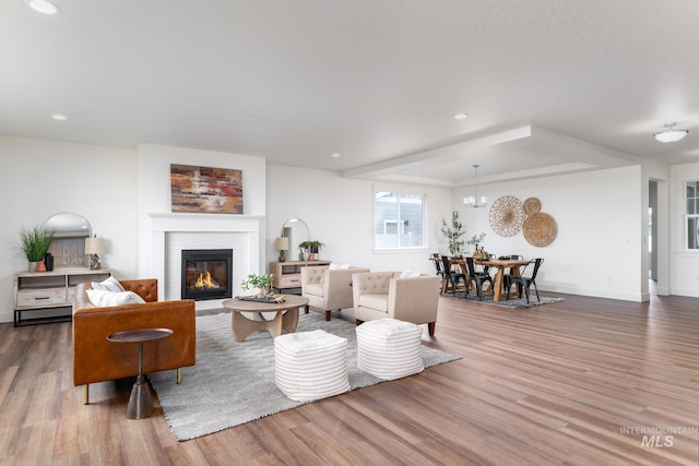 living room with baseboards, recessed lighting, an inviting chandelier, wood finished floors, and a glass covered fireplace