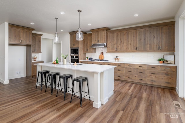 kitchen featuring visible vents, dark wood-type flooring, under cabinet range hood, appliances with stainless steel finishes, and a sink