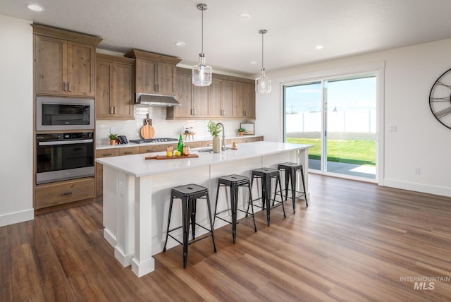 kitchen featuring a breakfast bar area, stainless steel appliances, light countertops, under cabinet range hood, and backsplash