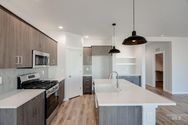 kitchen with stainless steel appliances, a kitchen island with sink, light countertops, and decorative light fixtures