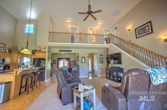 living room with light wood-type flooring, ceiling fan, and a towering ceiling