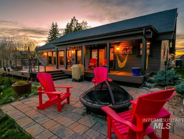 986 Valley Rim Rd, Mccall, ID 83638 - back of property at dusk featuring a fire pit, a patio, roof with shingles, and a wooden deck