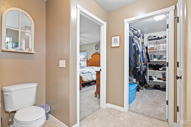 ensuite bathroom featuring baseboards, toilet, and a walk in closet