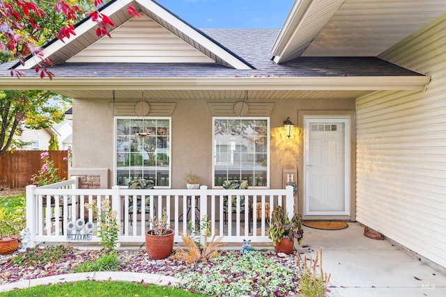 property entrance with covered porch, roof with shingles, stucco siding, and fence