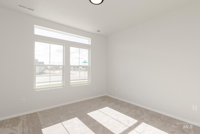 spare room featuring visible vents, a healthy amount of sunlight, light colored carpet, and baseboards