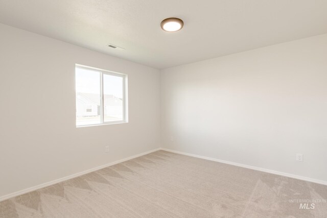 spare room with baseboards, light carpet, and visible vents