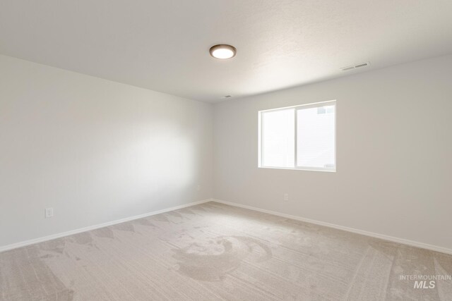 spare room featuring light colored carpet, baseboards, and visible vents