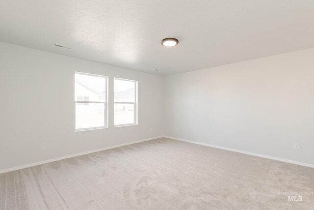 empty room featuring visible vents, light carpet, and baseboards