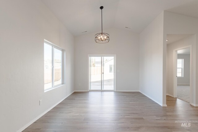 empty room with baseboards, light wood-style floors, an inviting chandelier, and high vaulted ceiling