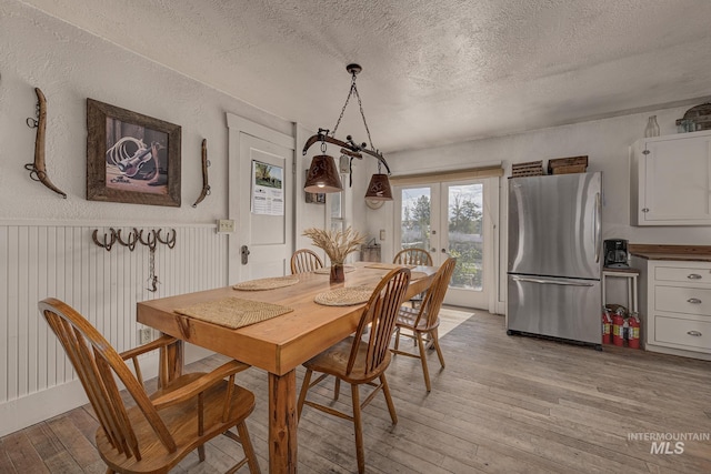 1507 Scheloske Rd, Weiser, ID 83672 - dining area featuring french doors, light wood-type flooring, a textured ceiling, and wainscoting