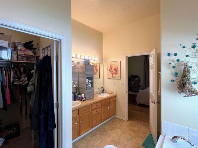 ensuite bathroom with ensuite bath, a spacious closet, a sink, lofted ceiling, and double vanity