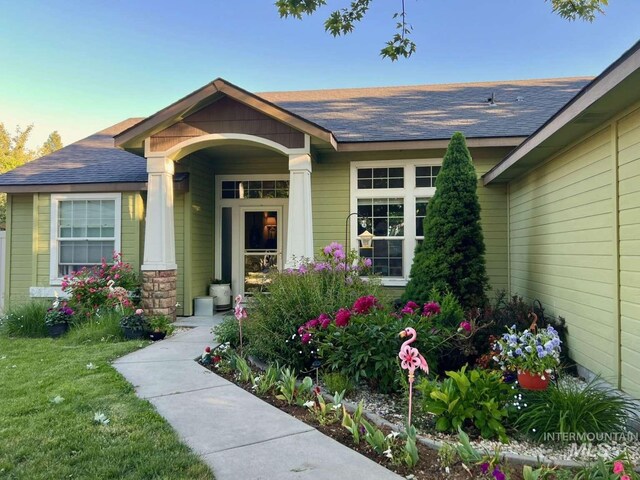 entrance to property featuring a yard, a shingled roof, and stone siding