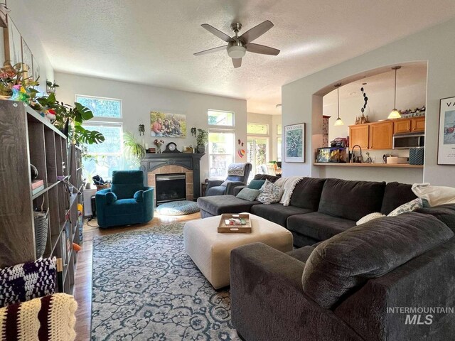 living room featuring a textured ceiling, wood finished floors, ceiling fan, and a fireplace