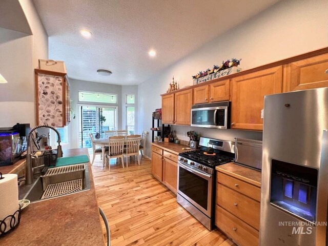 kitchen with light wood-style floors, brown cabinetry, a textured ceiling, a sink, and stainless steel appliances