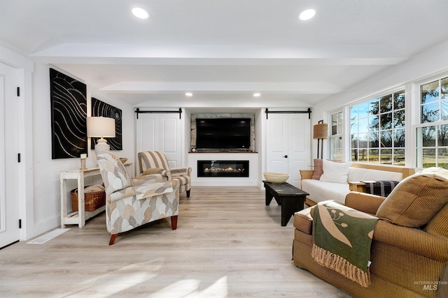 living room with beamed ceiling, light wood-type flooring, a large fireplace, and a barn door