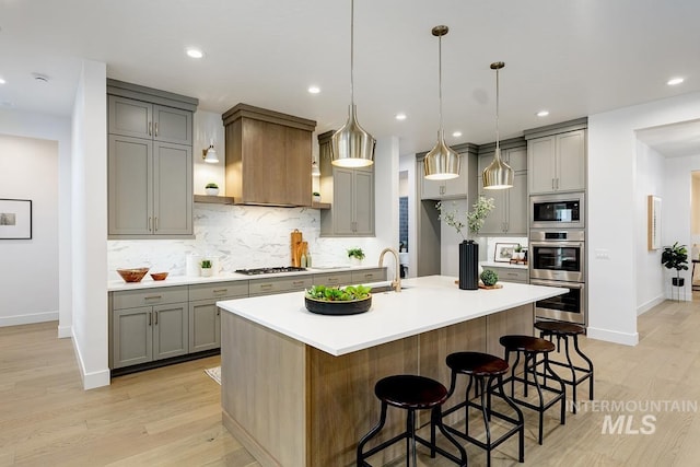 kitchen featuring tasteful backsplash, a breakfast bar area, a kitchen island with sink, stainless steel appliances, and light hardwood / wood-style flooring