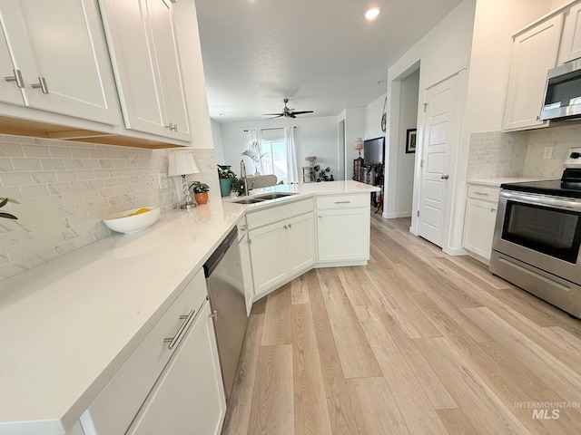 kitchen with light wood-style flooring, a peninsula, a sink, light countertops, and appliances with stainless steel finishes