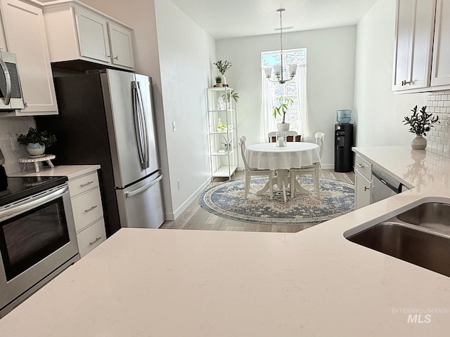 kitchen featuring a notable chandelier, light wood finished floors, backsplash, appliances with stainless steel finishes, and white cabinetry