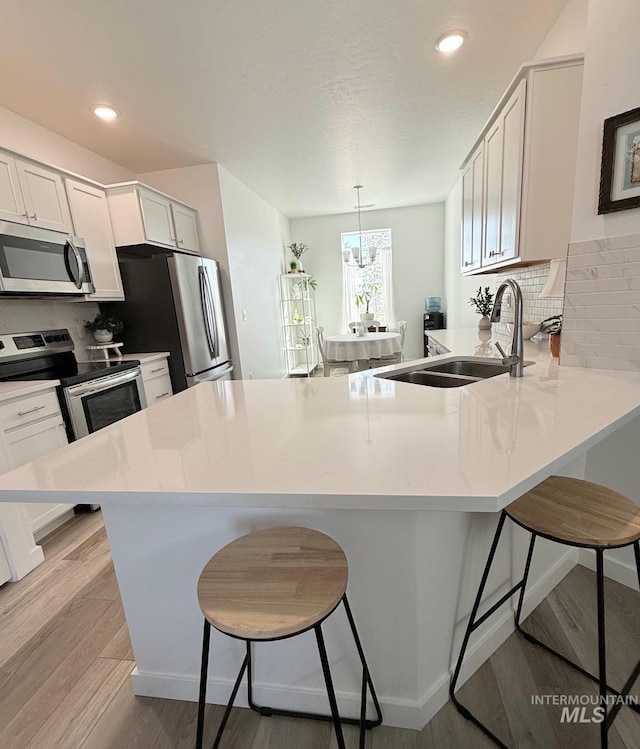 kitchen featuring a breakfast bar area, stainless steel appliances, a sink, light wood-type flooring, and a peninsula