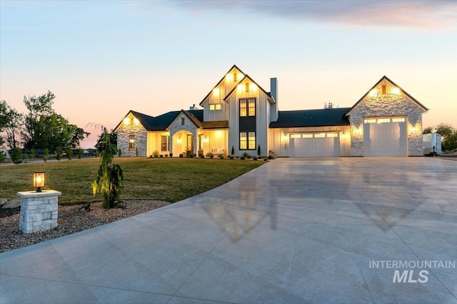 modern inspired farmhouse with a garage, driveway, stone siding, a front lawn, and board and batten siding