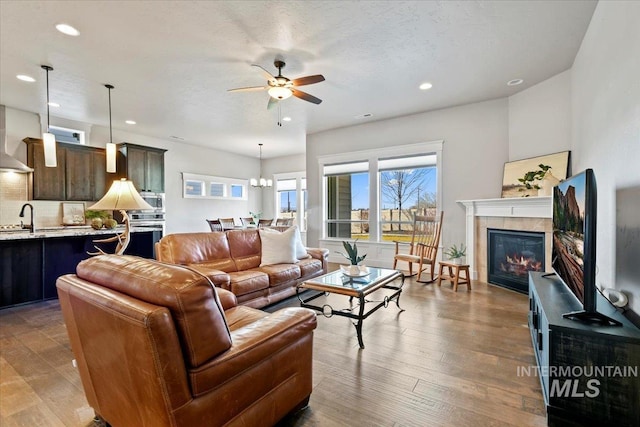 living room featuring a fireplace, ceiling fan with notable chandelier, light hardwood / wood-style floors, and sink