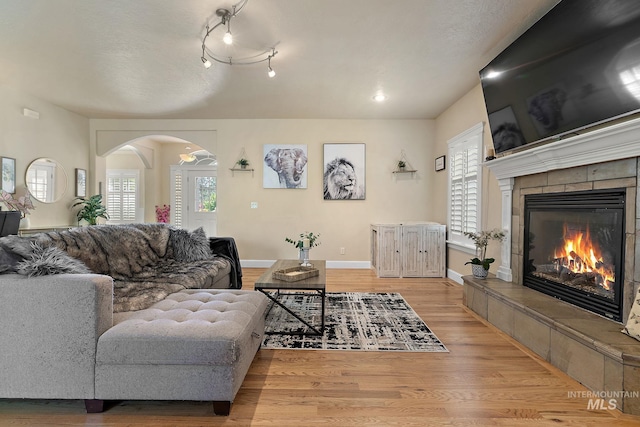 6114 N Cape Arago Pl, Boise, ID 83714 - living room featuring arched walkways, light wood-type flooring, a tiled fireplace, and baseboards