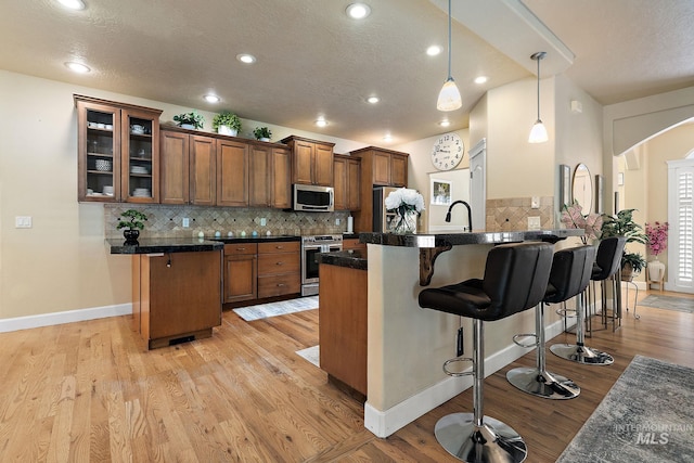 6114 N Cape Arago Pl, Boise, ID 83714 - kitchen with appliances with stainless steel finishes, a peninsula, a breakfast bar, brown cabinets, and a textured ceiling