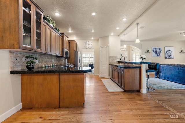 6114 N Cape Arago Pl, Boise, ID 83714 - kitchen with appliances with stainless steel finishes, a peninsula, a breakfast bar area, glass insert cabinets, and decorative backsplash
