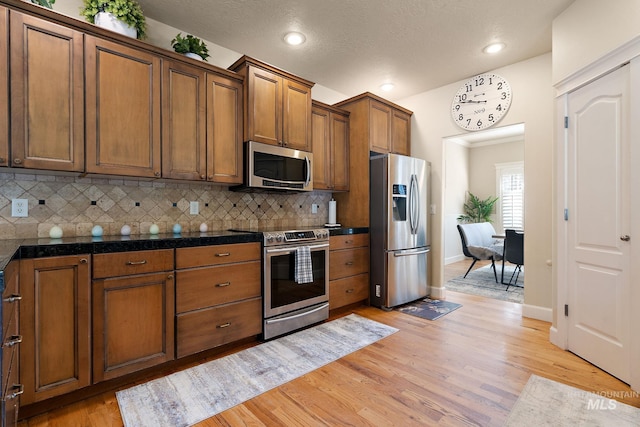 6114 N Cape Arago Pl, Boise, ID 83714 - kitchen featuring stainless steel appliances, brown cabinets, light wood-style flooring, decorative backsplash, and baseboards