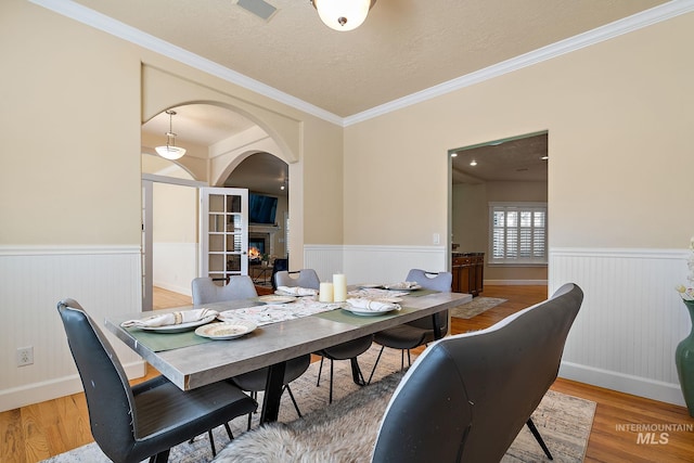 6114 N Cape Arago Pl, Boise, ID 83714 - dining space featuring a wainscoted wall, a glass covered fireplace, light wood-type flooring, arched walkways, and crown molding