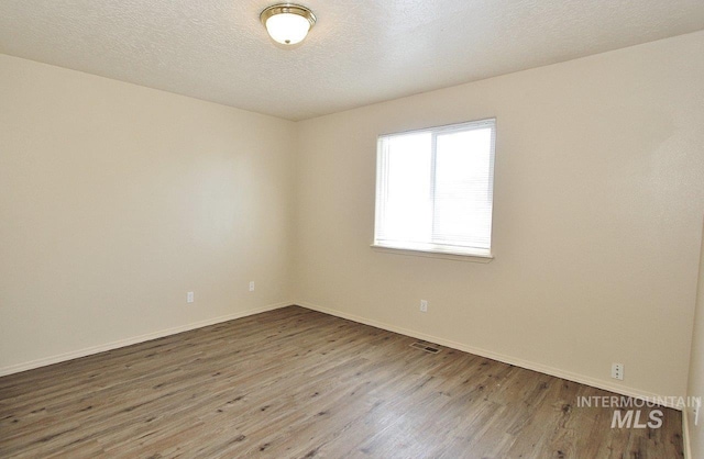 empty room featuring baseboards, wood finished floors, and visible vents
