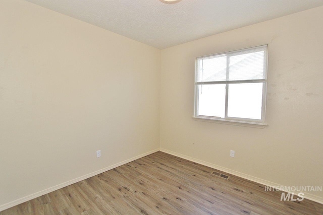 empty room featuring baseboards, light wood finished floors, and visible vents