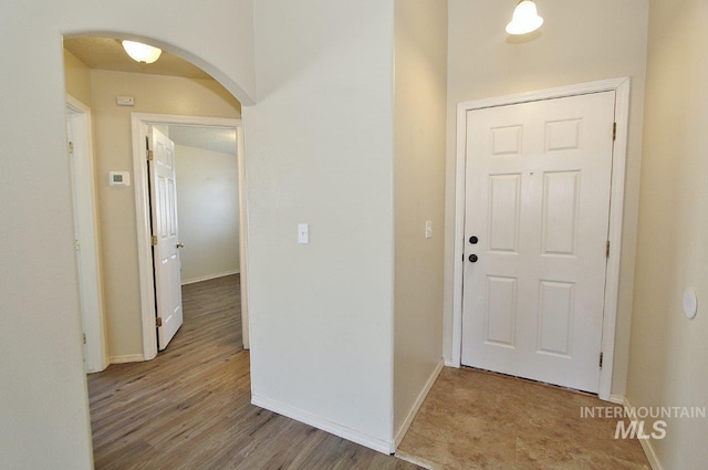 hall with arched walkways, baseboards, and wood finished floors