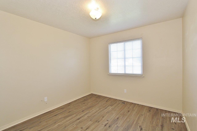 spare room featuring baseboards, wood finished floors, and visible vents