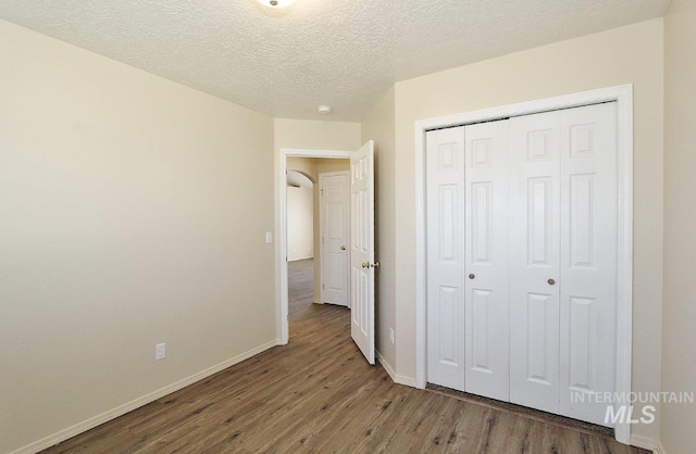 unfurnished bedroom featuring baseboards, a textured ceiling, wood finished floors, and a closet