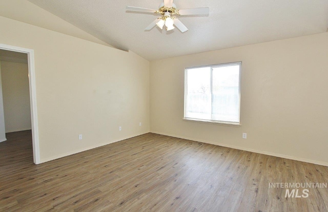 spare room with baseboards, a ceiling fan, wood finished floors, and vaulted ceiling