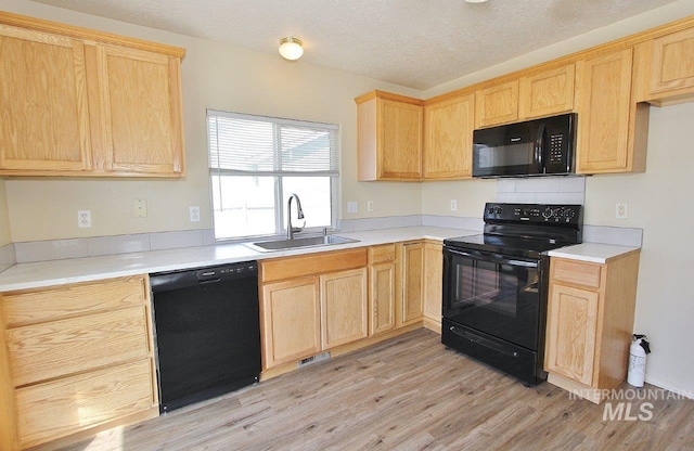 kitchen featuring light brown cabinetry, a sink, light countertops, black appliances, and light wood finished floors