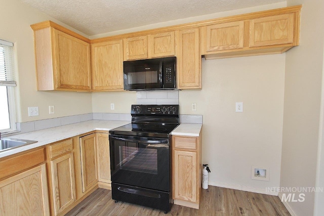 kitchen with light countertops, a sink, wood finished floors, and black appliances
