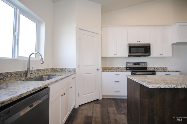 kitchen featuring stainless steel appliances, white cabinets, lofted ceiling, light stone counters, and sink