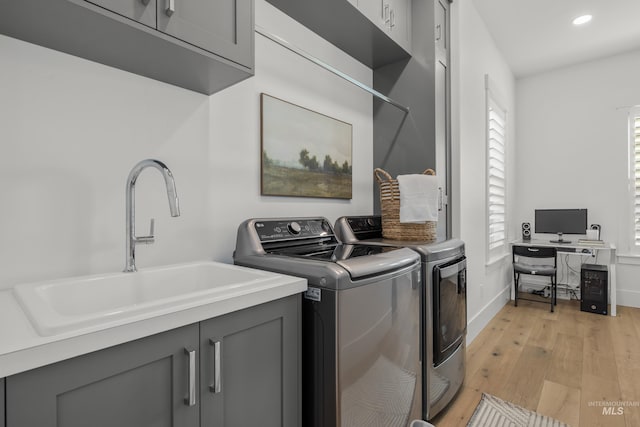 washroom with washer and dryer, light wood-type flooring, cabinets, and sink