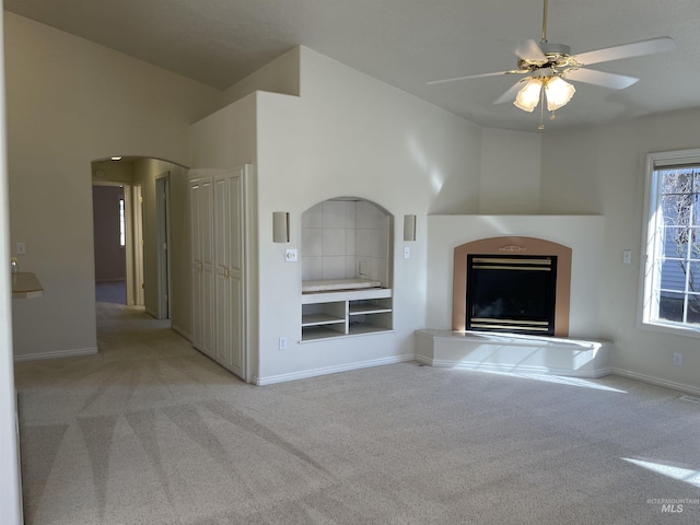 6064 N Lake Shore Ave, Garden City, ID 83714 - unfurnished living room featuring light carpet, baseboards, arched walkways, a ceiling fan, and a glass covered fireplace