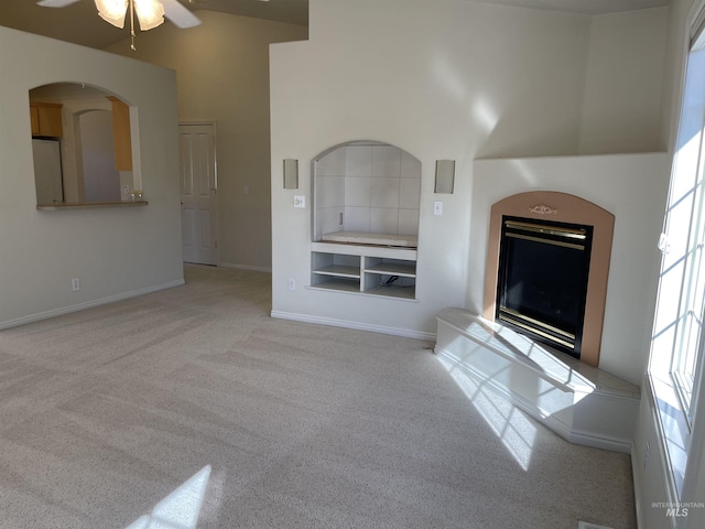 6064 N Lake Shore Ave, Garden City, ID 83714 - unfurnished living room featuring light carpet, a ceiling fan, a towering ceiling, baseboards, and a glass covered fireplace