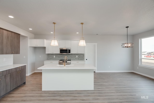 kitchen featuring appliances with stainless steel finishes, white cabinetry, hanging light fixtures, a center island with sink, and light hardwood / wood-style flooring