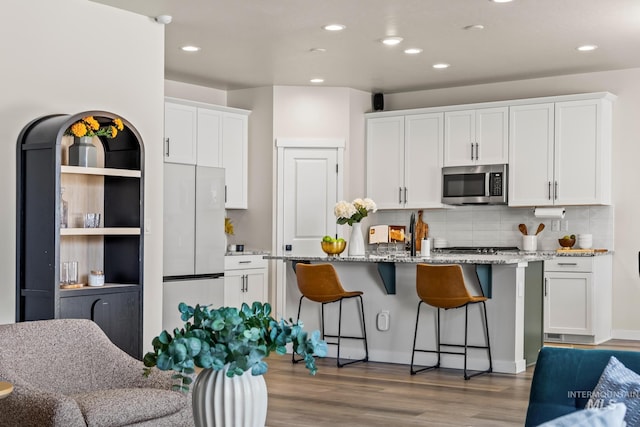 18293 N Begonia Way, Nampa, ID 83687 - kitchen with freestanding refrigerator, stainless steel microwave, white cabinetry, wood finished floors, and tasteful backsplash