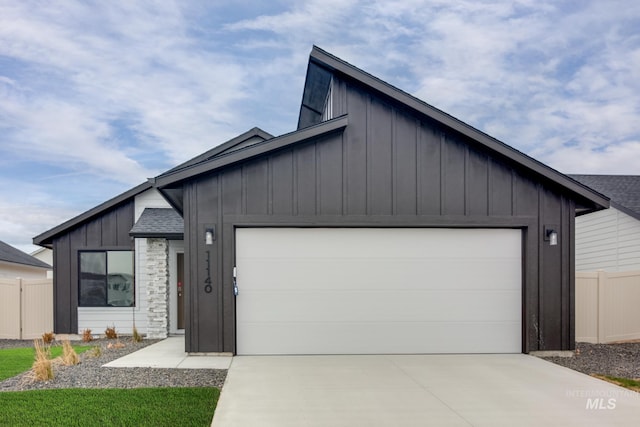 contemporary house with board and batten siding, fence, a garage, stone siding, and concrete driveway