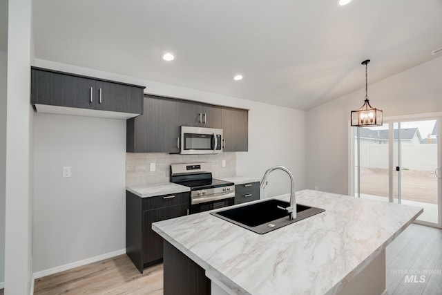 kitchen with light wood-style flooring, a sink, hanging light fixtures, appliances with stainless steel finishes, and tasteful backsplash