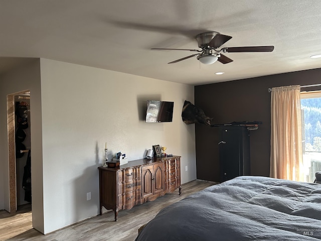 bedroom with a walk in closet, light hardwood / wood-style floors, a closet, and ceiling fan