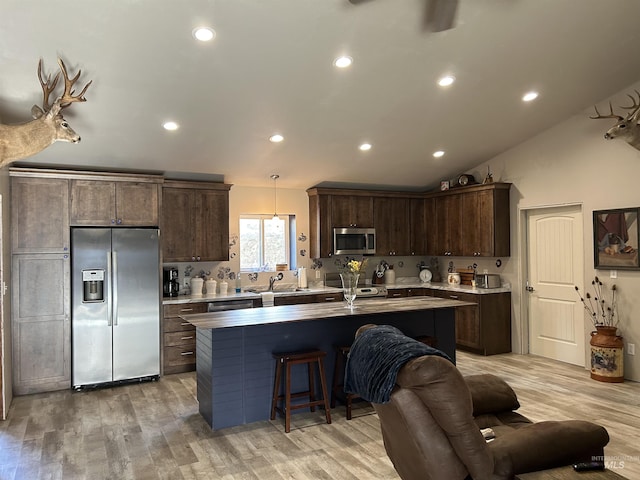 kitchen featuring appliances with stainless steel finishes, pendant lighting, dark brown cabinetry, a center island with sink, and light wood-type flooring