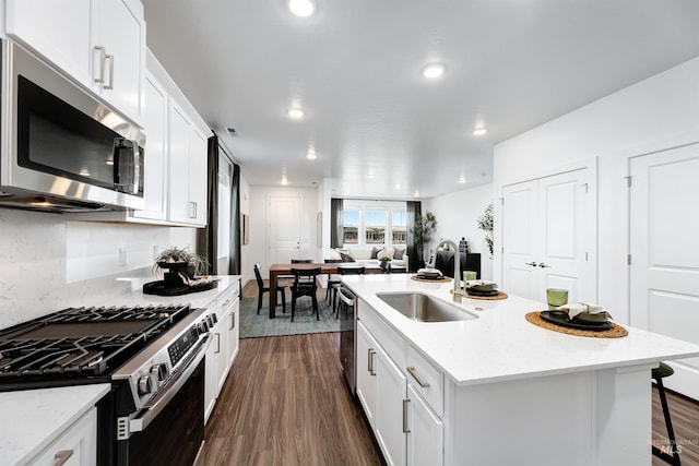 kitchen with sink, a breakfast bar, stainless steel appliances, light stone countertops, and a center island with sink