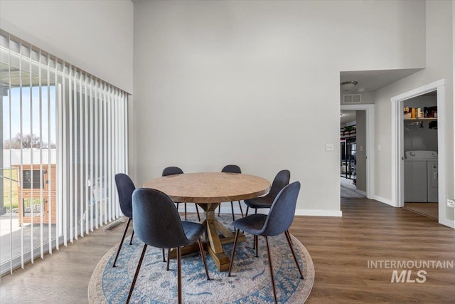 dining space with visible vents, baseboards, a high ceiling, and wood finished floors